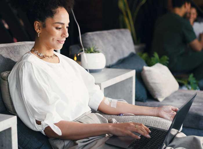 Woman, relax and laptop in clinic, iv drip and happy for recovery with fluid, writer and remote work. Healthcare, nutrition and person with tech for freelance article, typing and immune system boost